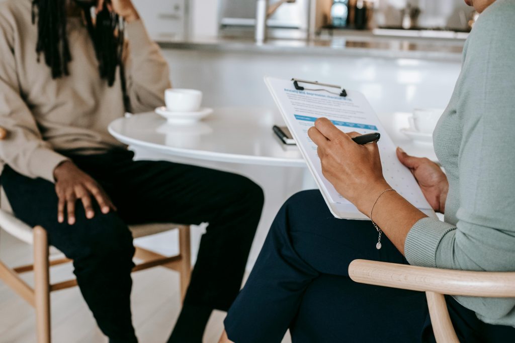 person sitting at table with clipboard, interviewing someone else at the table