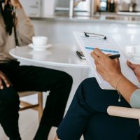 person sitting at table with clipboard, interviewing someone else at the table